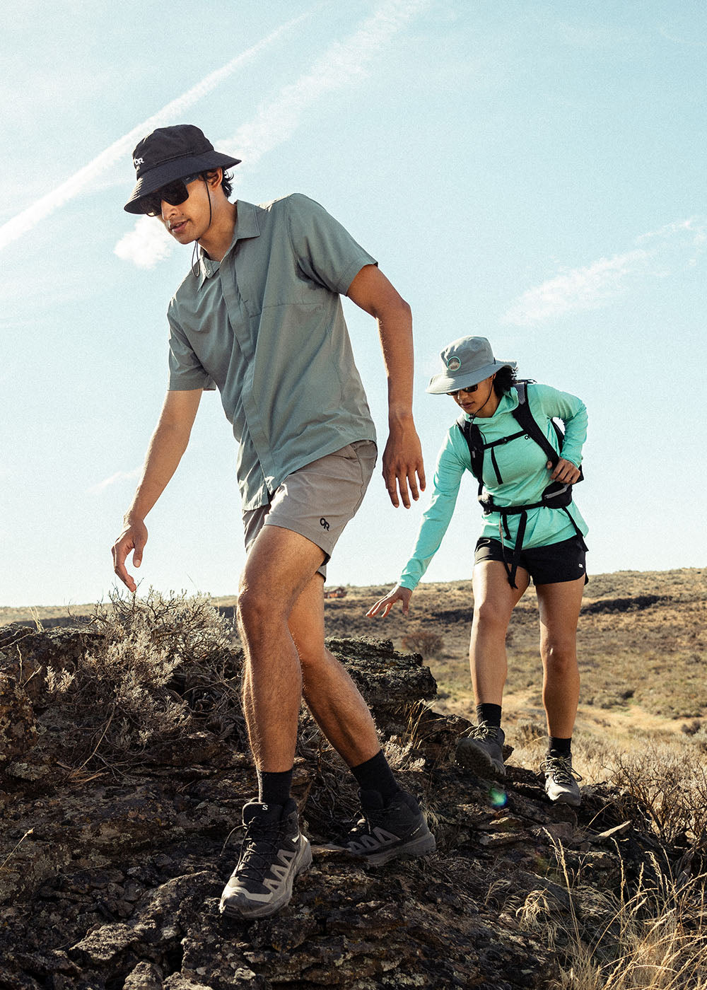 Two friends balance on rock as they hike in the sun wearing Outdoor Research sportswear. 